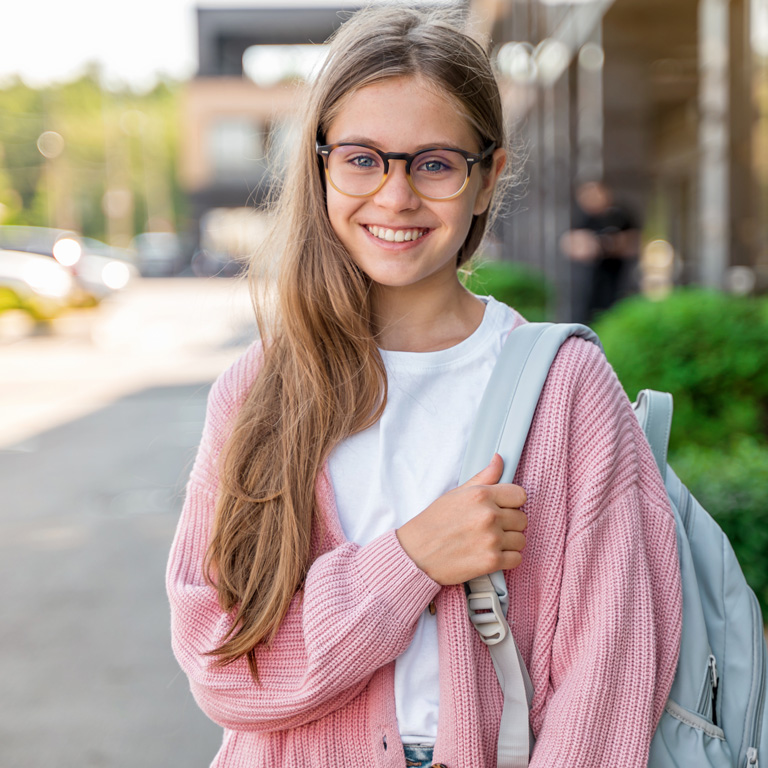 young girl wearing glasses and backpack smiling at camera