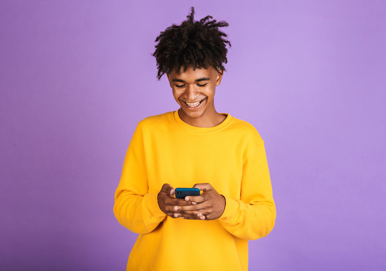 young teen smiling at his phone in front of purple background